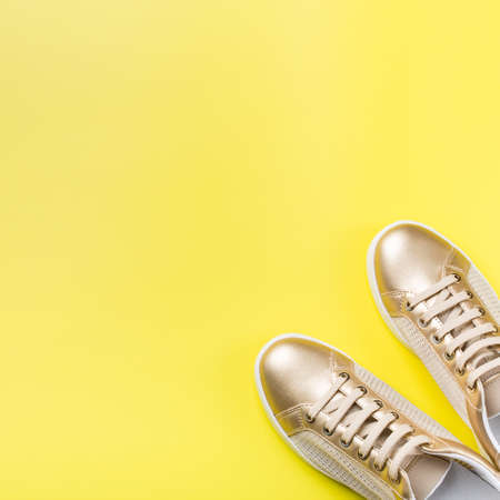 Fashion, blog, blogging, lifestyle, well-being trendy concept. Pair of golden female sneakers on yellow background, top view, copy space, flat layの写真素材