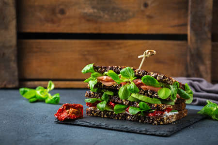 Food, breakfast, morning and lunch concept. Fresh healthy rye bread sandwich with ham, lettuce and dried tomato on a tableの写真素材
