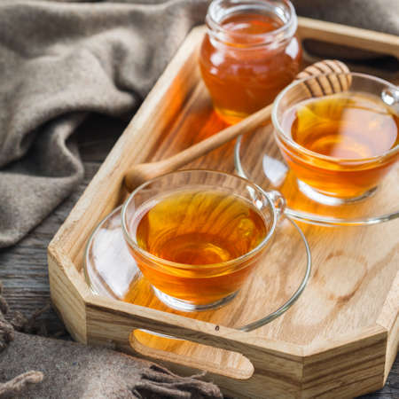 Autumn, fall, winter home decor in hygge style with drink. Seasonal composition with cup of hot tea with honey, warm woolen scarf, soft plaid on a rustic wooden table.の写真素材