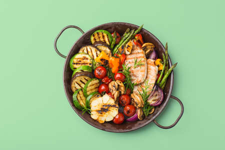 Seasonal, summer eating concept. Grilled vegetables and chicken breast in a pan on a trendy neo mint...