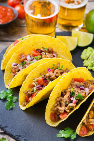 Taco shell ellow corn tortilla chips nachos with ground beef, mince, guacamole, red hot jalapeno chili salsa and cheese sauce with tequila or beer on a table.の写真素材