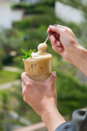 Hands holding trendy Dalgona Coffee on the balcony, outdoor. Iced frothy whipped ultra fluffy texture. Viral social media worthy drink in coronavirus, Covid-19, lockdown, quarantine, stay at home.の写真素材