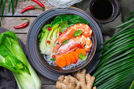 Food and drink, traditional asian cuisine. Spicy bee hoon, bihun soup with shrimp, prawn, boy choy and rice vermicelli noodles on a wooden table. Top view flat lay background の写真素材
