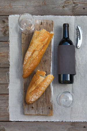 Food, still life composition. Picnic, romantic meal with french baguette, wine glasses and red wine in bottle on a rustic wooden table. Top view flay lay backgroundの写真素材