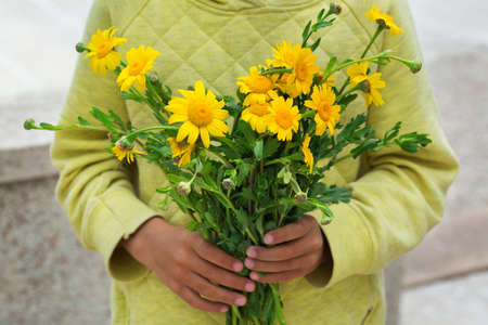 Young boy, kid, child holding in hands bouquet of yellow wild flowers. Gift for mother conceptの写真素材