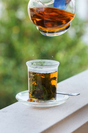 Drink for stress, anxiety, chronic fatigue, depression relieving and relaxation. Glass of hot mint tea with cane sugar, traditional Middle East, moroccan, arabic, moorish beverage pouring from teapotの写真素材