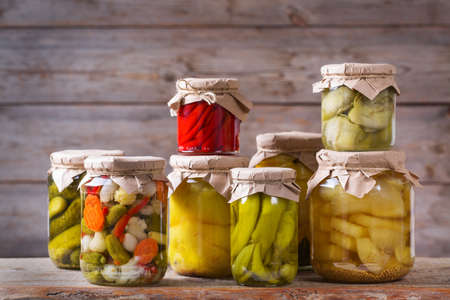 Preserved and fermented food. Assortment of homemade jars with variety of pickled and marinated vegetables on a wooden table. Housekeeping, home economics, harvest preservation  の写真素材