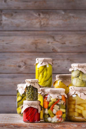 Preserved and fermented food. Assortment of homemade jars with variety of pickled and marinated vegetables on a wooden table. Housekeeping, home economics, harvest preservation  の写真素材