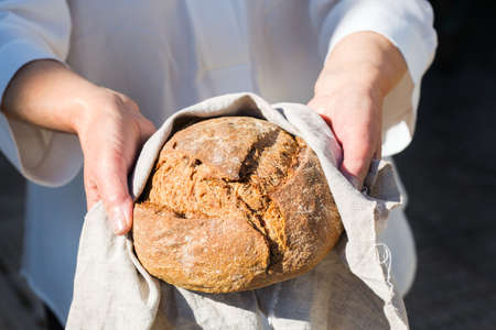Mature senior woman holding freshly baked loaf of homemade rye bread in her hands