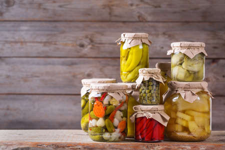 Preserved and fermented food. Assortment of homemade jars with variety of pickled and marinated vegetables on a wooden table. Housekeeping, home economics, harvest preservation  の写真素材