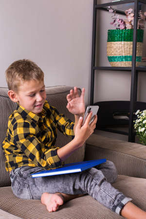 Cute smiling boy talking with family and friends, making video call on the phone, sitting on a...