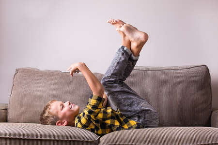 Cute smiling boy talking with family and friends, making video call on the phone, sitting on a couch. Stay at home, lockdown, social distancing, quarantine.の写真素材