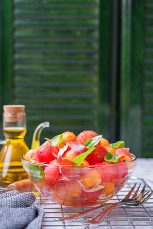 Healthy clean eating, dieting and nutrition, seasonal, summer meal lunch concept. Fruit salad with melon cantaloupe, watermelon and prosciutto in a bowl on a kitchen table.の写真素材