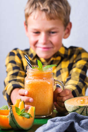 Cute happy boy drinking healthy orange smoothie with straw. Little kid, child enjoying his drink, smiling and laughing.の写真素材
