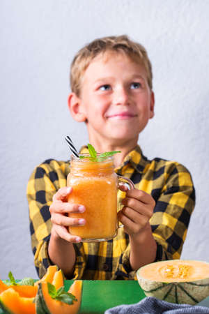 Cute happy boy drinking healthy orange smoothie with straw. Little kid, child enjoying his drink, smiling and laughing.の写真素材