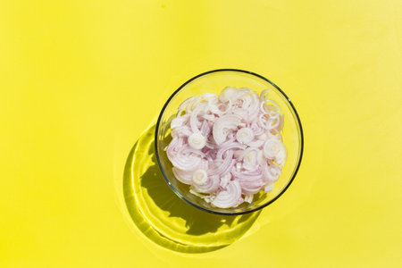 Sliced red onion rings with sunny, vivid, hard light and shadows. Creative pop art design concept. Trendy copy space illuminating yellow backgroundの写真素材