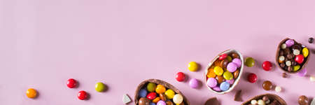 Easter frame with chocolate eggs and sweets on a pink background. Banner, top view, flat lay