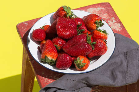 Plate with fresh red strawberries on a yellow in sunny day with shadowsの写真素材