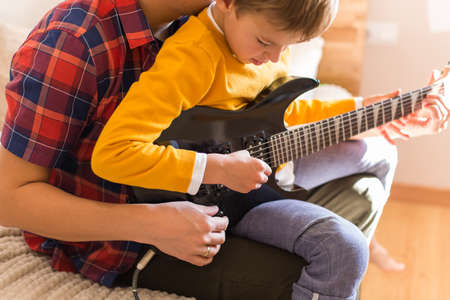 Young millennial man, father and cute son playing electric guitar. Stay at home, home activity, learning classes, family having fun time togetherの写真素材