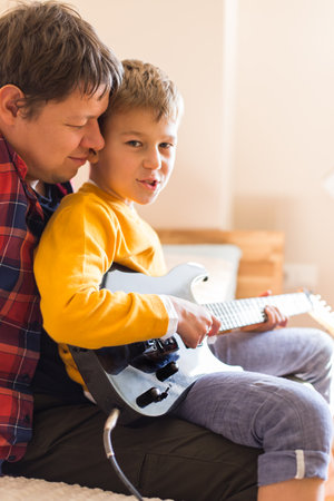 Young millennial man, father and cute son playing electric guitar. Stay at home, home activity, learning classes, family having fun time togetherの写真素材