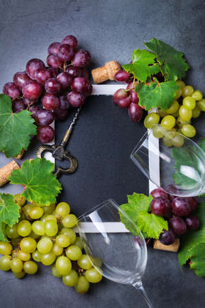Food and drink, harvest autumn fall concept. Wine tasting, degustation, invitation card with symbols - grape vine, bottle, glasses, corkscrew. Copy space black backgroundの写真素材