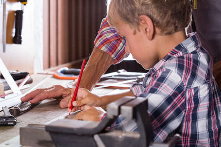 Grandfather teaches boy to work on bench with joinery tools