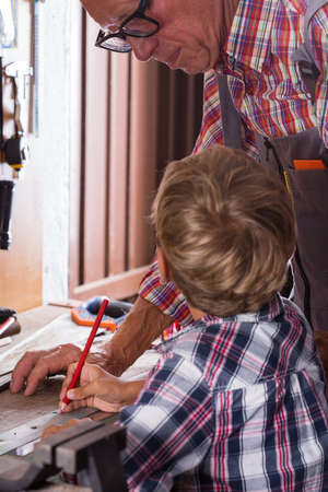 Grandfather teaches boy to work on bench with joinery tools