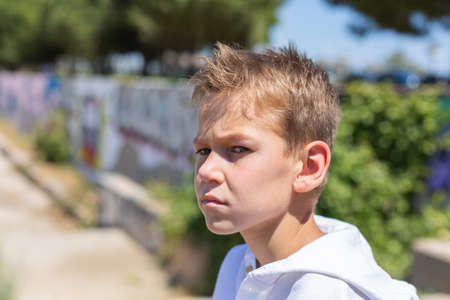 Handsome young boy, teenager is sitting outdoors and looking aroundの写真素材