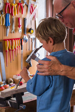 Grandfather teaches boy to work on bench with joinery toolsの写真素材