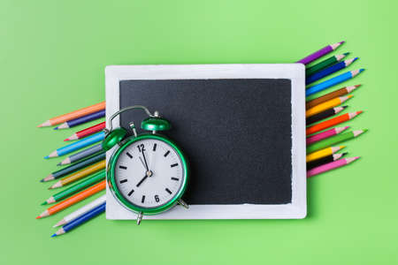 Colourful rainbow pencils and alarm clock on lime green backgroundの写真素材