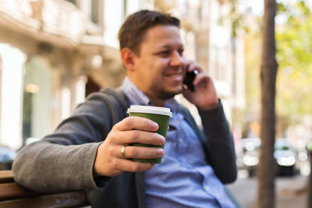 Man walking on the street, drinking coffee, talking by phoneの写真素材