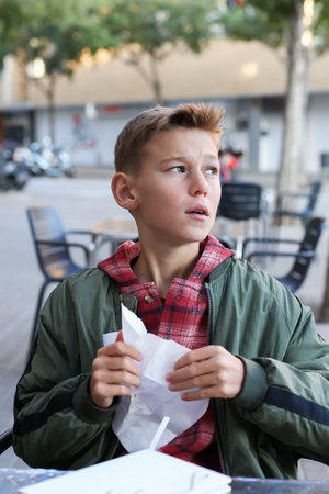 Handsome teenager blowing nose and sneezing sitting in outdoor cafe. Caucasian young boy is suffering from fluの写真素材