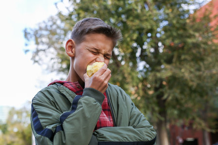 Teenager eating green apple on the city street, outdoors. Young boy is waiting his friends for a walkの写真素材