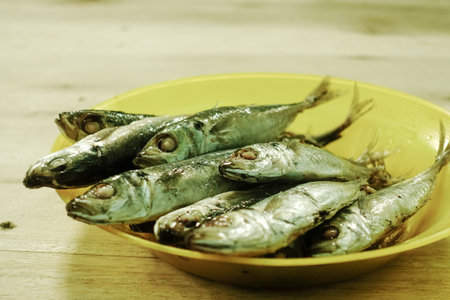 Fried mackerel fish in yellow bowl on wooden table.の写真素材