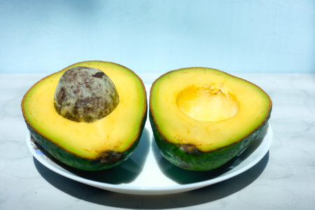 Avocado fruit cut in half on a plate on a blue background