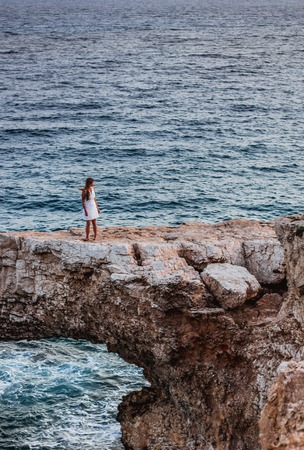 Woman in white dress on the beautiful natural rock arch near of Ayia Napa, Cavo Greco and Protaras on Cyprus island, Mediterranean Sea. Legendary bridge lovers.の写真素材