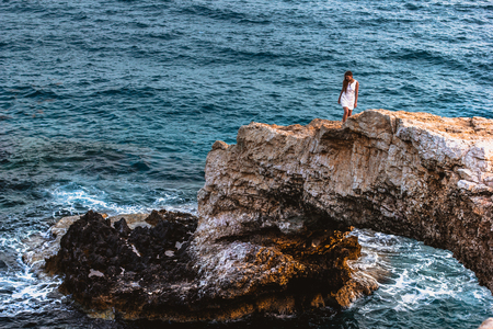 Woman in white dress on the beautiful natural rock arch near of Ayia Napa, Cavo Greco and Protaras on Cyprus island, Mediterranean Sea. Legendary bridge lovers.の写真素材