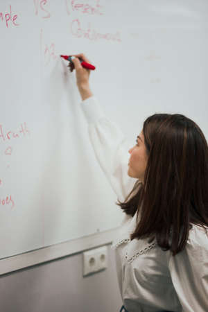 Female teacher writing on the marker board im classroom. Education concept english language lesson