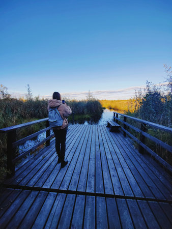 Young woman standing on a wooden pier and taking photo of a large crayfish lake. State Natural Reserve Cancer Lakes , St. Petersburgの写真素材
