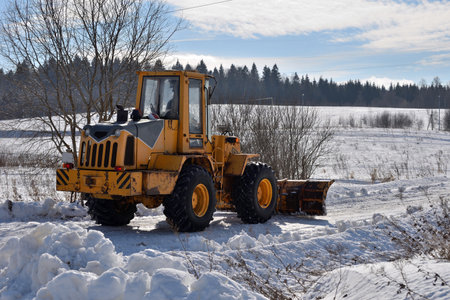 Tractor clears road in village on winter sunny day