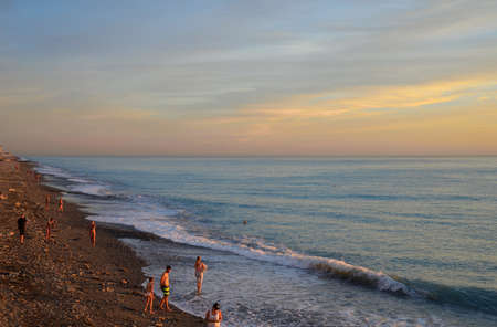 Beach and people swimming in sea waves at sunset in Loo village, Sochi, Krasnodar Region, Russiaの写真素材