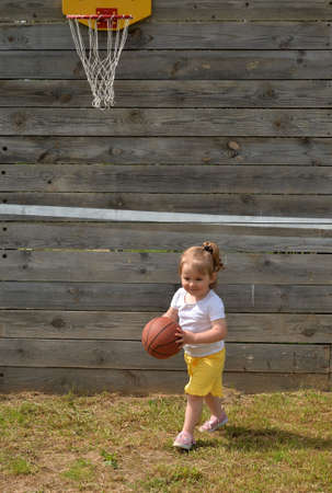 Little girl plays basketball on lawn in summerの写真素材
