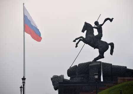 Statue of St. George Victorious at foot of main Victory obelisk and flag of Russian Federation in Poklonnaya Hill in heavy fog, Moscow, Russiaのeditorial素材