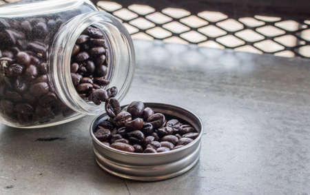 Close up of coffee beans in bottle cap and bottle on concrete floor at the coffee shop with copy...