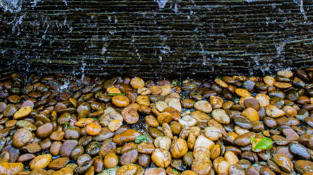Close up of waterfall on stone wall and colorful pebble on ground in the garden.の写真素材