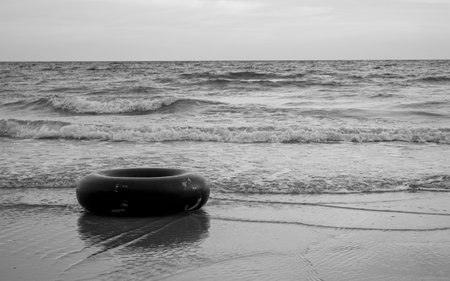 Monochrome of Black swim ring on the beach in black and white tone. Rubber ring floating in the sea with copy space.の写真素材