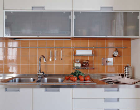 detail of a modern kitchen with vegetables on the steel worktop near to steel sink and orange tile wallの写真素材