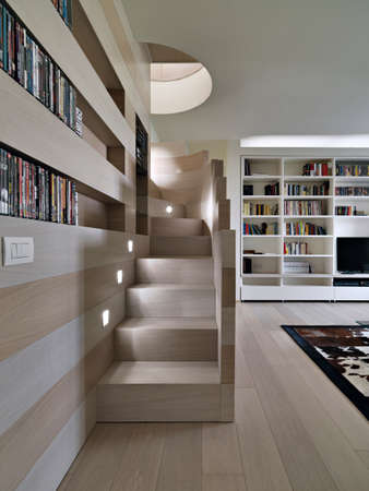 modern living room in foreground the wooden staircase overlooking on the big bookcase whose floor isa mde of woodの写真素材
