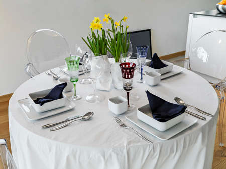 table set with white ceramic plates, blue napkins and centerpieces of fresh yellow flowers with colored glassesの写真素材