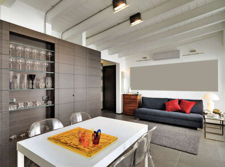 interior view of a modern living room in foreground the dining table overlooking on the entrance and sofa in the attic roomの写真素材